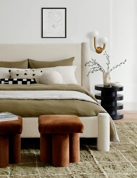 A high-end lifestyle shot featuring a cream-colored upholstered bed with textured bedding in earthy olive tones, styled with modern bedside decor.