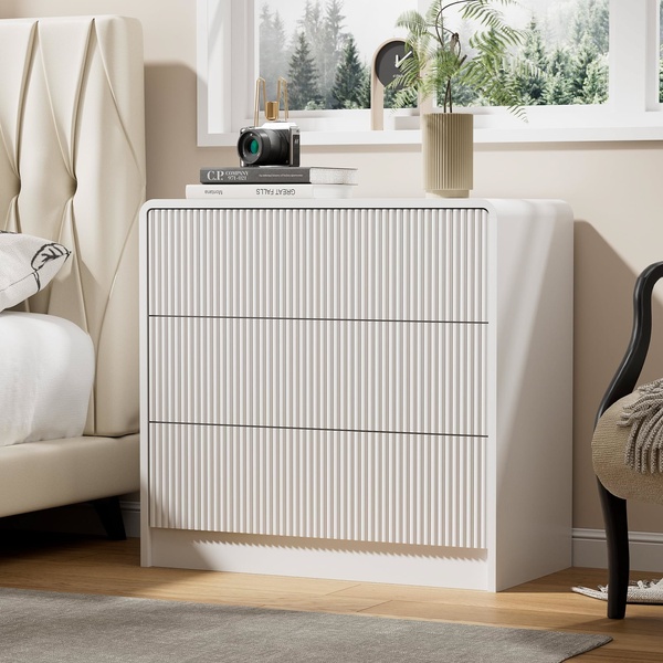 A high-end product photography shot of a textured white three-drawer nightstand in a bright, serene bedroom setting.