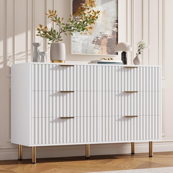 A high-end, clean-focused product shot of a white fluted-front dresser styled in a minimalist bedroom setting.