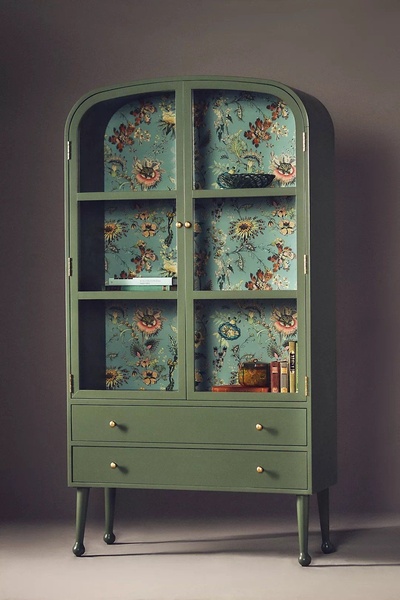 A high-quality studio shot of a green display cabinet with floral interior wallpaper, presented against a clean, neutral background.