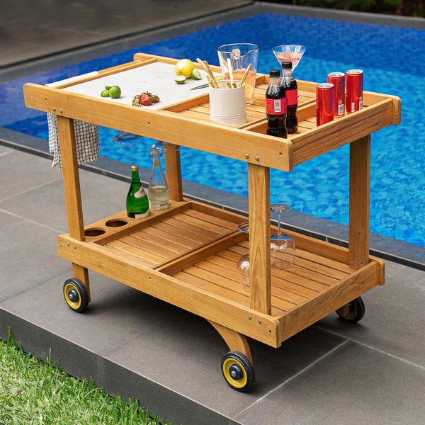 A high-quality lifestyle photograph of a wooden bar cart placed beside a blue swimming pool, showcasing outdoor entertainment.