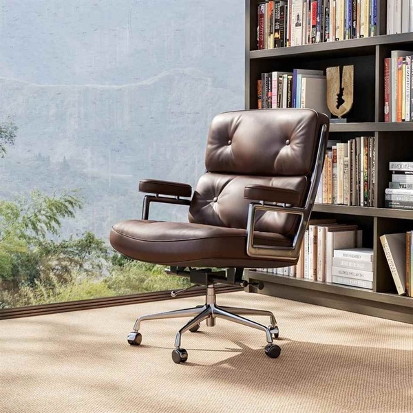 A high-quality leather office chair is positioned in a sophisticated home study setting with a bookshelf and natural light.