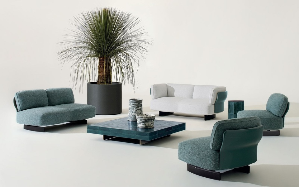 A high-end furniture arrangement featuring a white and teal sofa set with a textured coffee table and an oversized yucca plant in a studio setting.