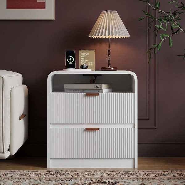 A clean, studio-lit photograph of a modern white bedside table featuring integrated wireless charging, styled in a luxurious, moody bedroom interior.