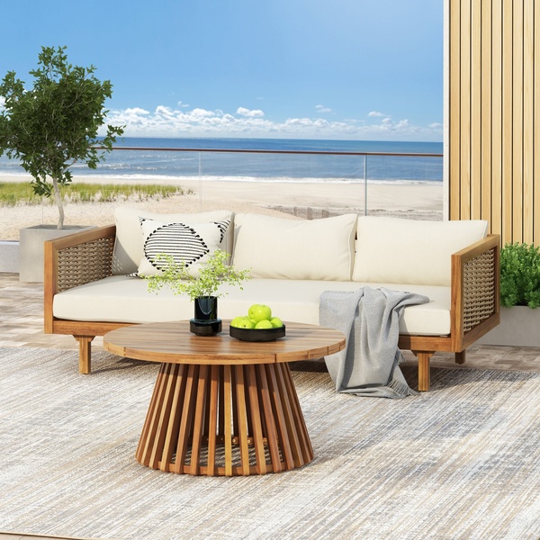 A high-end, lifestyle-focused shot of an outdoor sofa on a deck, featuring warm wood tones and neutral cushions against a beach background.