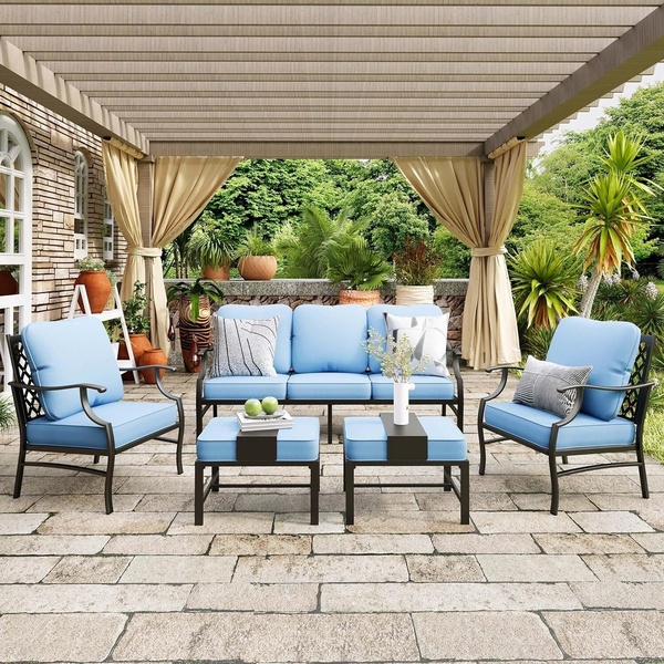 A high-quality lifestyle shot featuring a modern blue outdoor sofa set styled on a stone patio under a pergola.