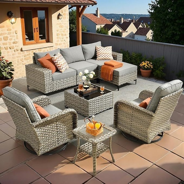 A clean, high-angle outdoor shot of a modular wicker sectional, fire-pit table, and swivel chairs arranged on a stone patio at dusk.