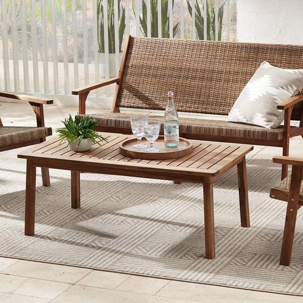 A high-quality lifestyle shot featuring an outdoor coffee table staged on a patterned rug, highlighting a balanced, inviting backyard environment.
