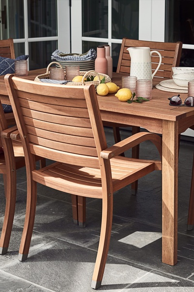A high-quality lifestyle shot featuring an outdoor dining chair in a sun-drenched patio setting, emphasizing organic textures and a relaxed mealtime atmosphere.
