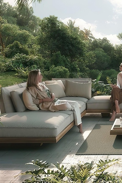 A high-end outdoor sectional sofa is displayed in a lush, natural environment, emphasizing comfort and premium relaxation through a soft, aspirational aesthetic.
