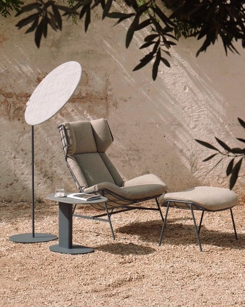 A high-quality lifestyle shot of a modern outdoor lounge chair with ottoman and matching side table set against a rustic stone wall.