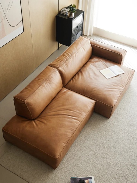 A high-angle, clean product shot of a tan leather sectional sofa placed in a modern, neutral-toned living space, focusing on premium materials.
