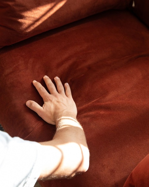 A top-down view showing a hand touching a deep red velvet sofa to emphasize texture and material quality.