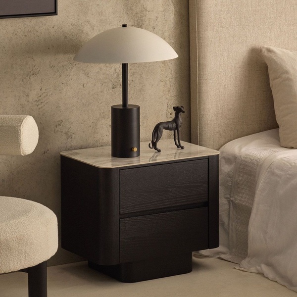 A high-end square composition featuring a black wood nightstand with a marble top, paired with a modern lamp and sculptural decor against a textured wall.