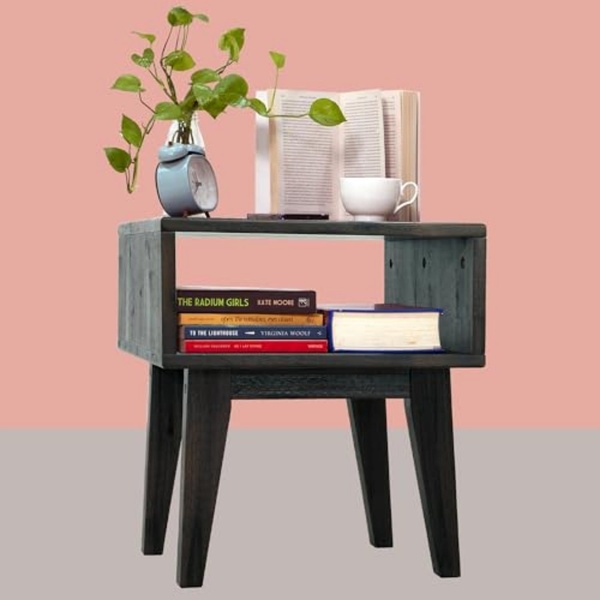 A clean, eye-level shot of a modern nightstand styled with books, a clock, and a plant against a soft-hued, solid background.