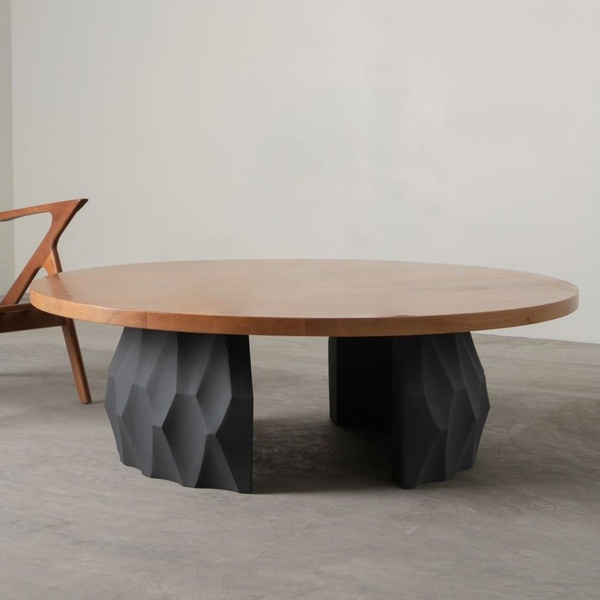 A minimalist, 1:1 ratio product shot highlighting a round wooden table top paired with a sculpted, matte black geometric base.