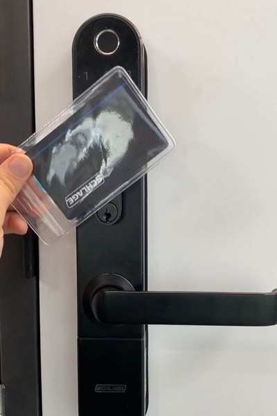 A close-up shot showing a hand using a digital access card to unlock a smart, biometric-enabled door handle.
