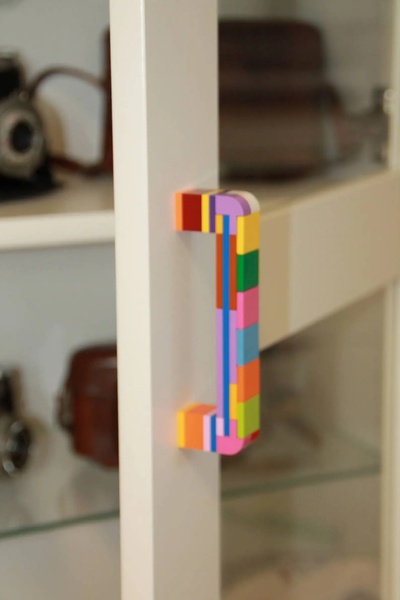 A close-up photograph showcasing a custom cabinet door handle constructed from colorful toy building bricks.