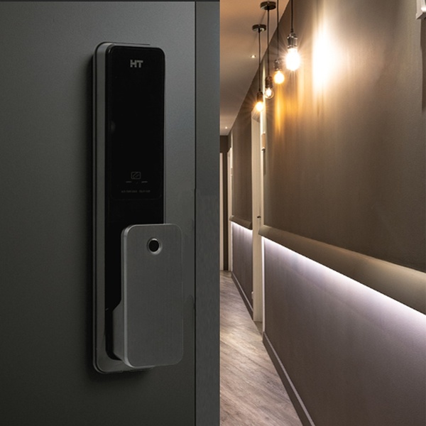 A high-quality 1:1 image featuring a smart door lock mounted on a modern door frame, contrasted with a warm, softly lit residential hallway.