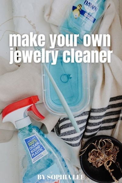 A clear, overhead shot showing a bowl of cleaning solution with a ring, a bottle of dish soap, and a dish of jewelry, focusing on a DIY cleaning method.