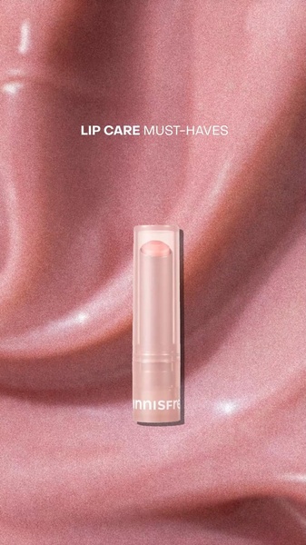 A close-up, high-texture product hero shot of a lip balm centered against a silky, soft-pink fabric background.