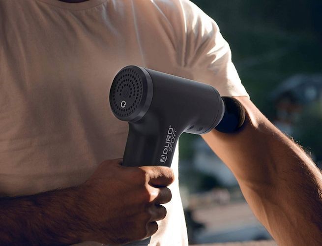 A close-up shot capturing a person using a massage gun on their arm, emphasizing the product's usability and physical relief benefits.