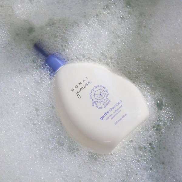 A close-up, high-quality shot of a Gentle Shampoo bottle floating in soapy bubble water to emphasize purity and safety.