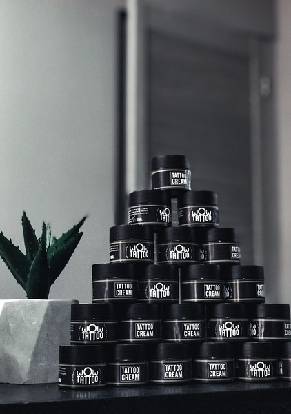 A symmetric, minimalist pyramid arrangement of multiple tattoo cream jars set against a neutral, moody background with a small succulent.