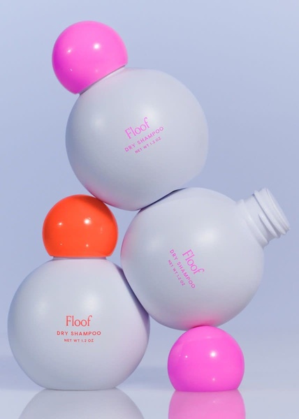 A high-key product photography shot featuring stacked dry shampoo bottles in a minimalist setting to highlight packaging and color contrast.
