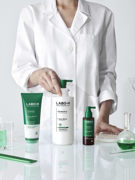 A professional in a white lab coat presents the scalp care product range, highlighting clinical efficacy through sterile, green-accented laboratory visuals.
