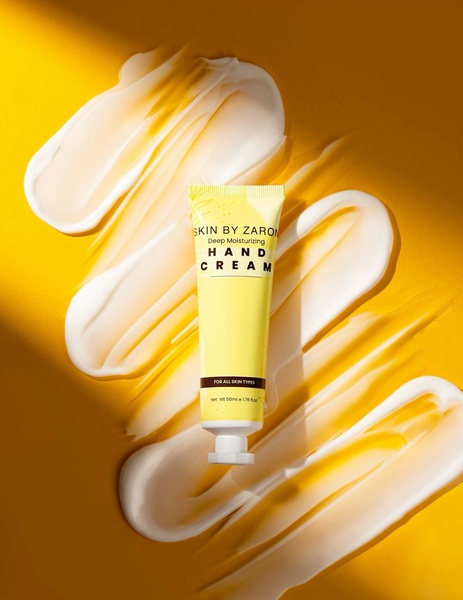 This creative showcases a hand cream tube centered amidst artistic, high-contrast cream swirls on a vibrant yellow background.