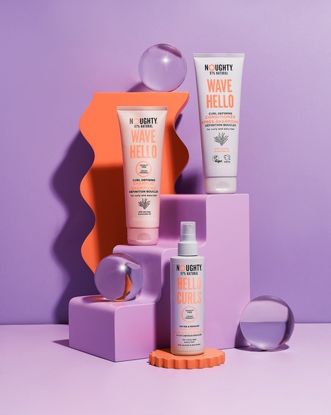 This creative showcases three curly hair care products arranged on geometric, wavy, and tiered platforms against a solid, vibrant background to emphasize a premium brand aesthetic.