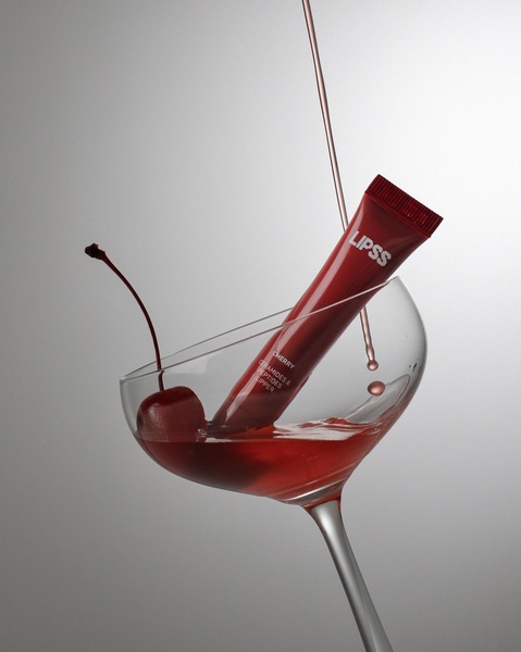 A refined product advertisement showcasing a cherry lip balm tube inside a martini glass with cherry juice, emphasizing a clean and luxurious aesthetic.