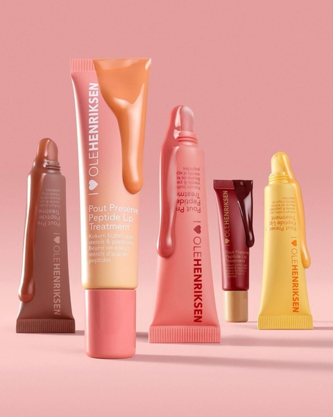 A high-end editorial shot featuring five tubes of lip treatment with product texture elegantly dripping from each nozzle against a soft pink background.