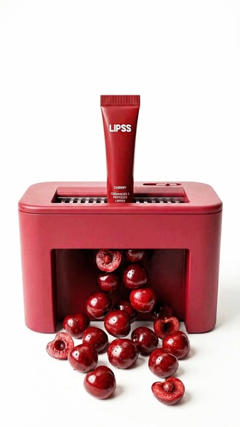 A high-contrast, studio-style shot featuring a lip treatment tube placed in a cherry pitting machine with cherries cascading out, highlighting ingredient-focused branding.