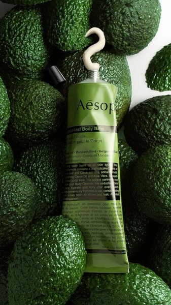 A close-up, high-texture product hero shot featuring body balm surrounded by fresh avocados to emphasize natural ingredients.