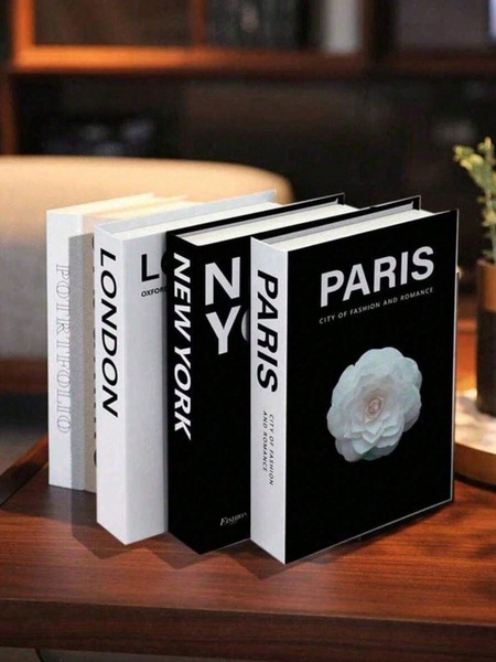 A high-end, clean product shot featuring a stack of four decorative books with city-themed labels and a delicate floral accent.