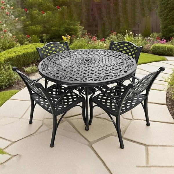 A high-quality, 1:1 square aspect ratio image of an ornate black metal outdoor dining set placed on a clean stone patio, surrounded by lush landscaping.