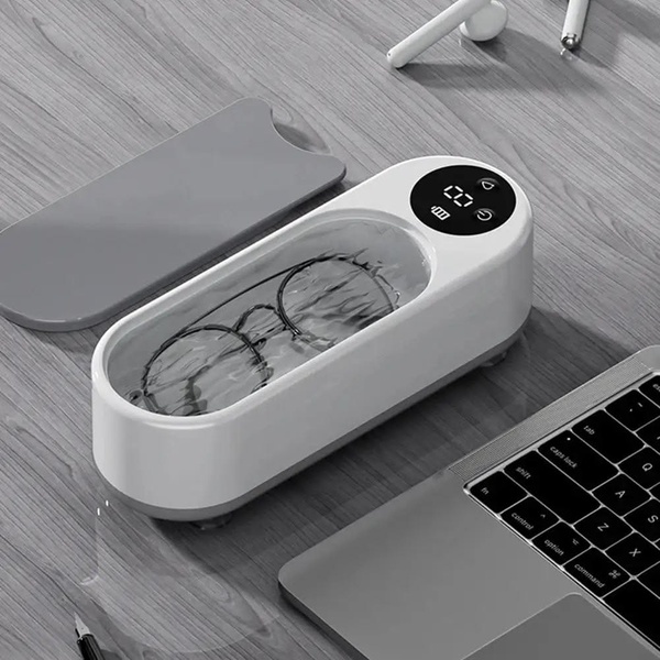A high-contrast, professional product shot of an ultrasonic cleaner submerged in water on a wooden desk, highlighting its clean design and premium feel.