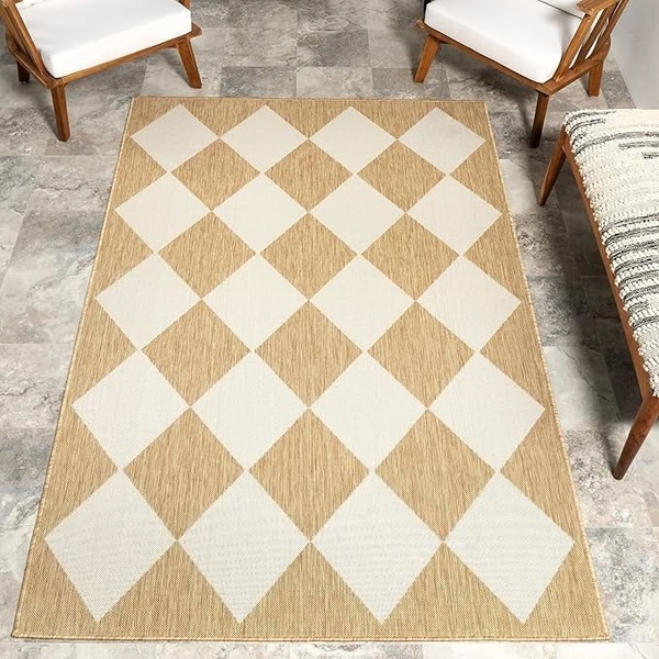 A top-down, clean product shot of a beige and white geometric diamond pattern area rug placed in a bright, modern living room space.