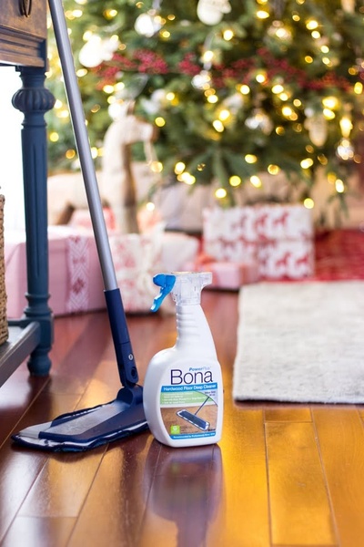 A high-quality studio-style product shot featuring a hardwood floor cleaner placed in front of a blurred Christmas tree.