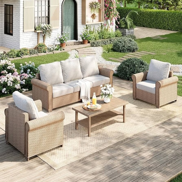 A high-quality, bright outdoor lifestyle shot of a complete wicker patio set placed on a wooden deck in front of a modern farmhouse.