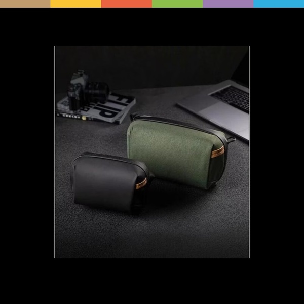 A clean, studio-lit shot of two tech travel pouches, one black and one olive, placed on a dark surface next to a laptop and camera to signal premium utility.