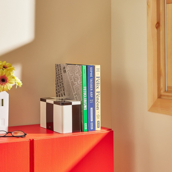 A clean, minimalist product hero shot featuring a checkered box and books on a bold red surface, creating a high-contrast visual focus.