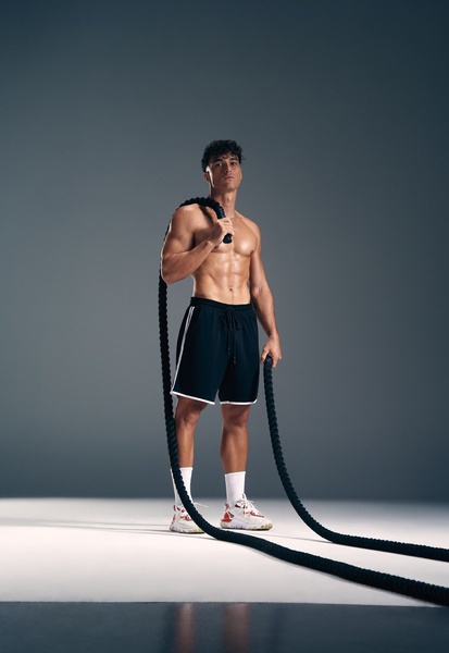 A high-contrast, professional studio portrait of an athletic male posing with heavy-duty training ropes to showcase strength and product quality.