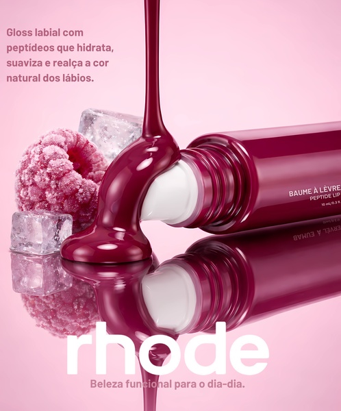 A close-up shot of liquid lip gloss pouring onto a smooth applicator, flanked by raspberries and ice cubes against a soft pink background.