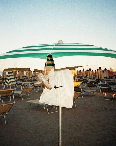 A running shoe is artfully hung from a green and white beach umbrella, utilizing a natural, high-contrast environment to showcase the product.