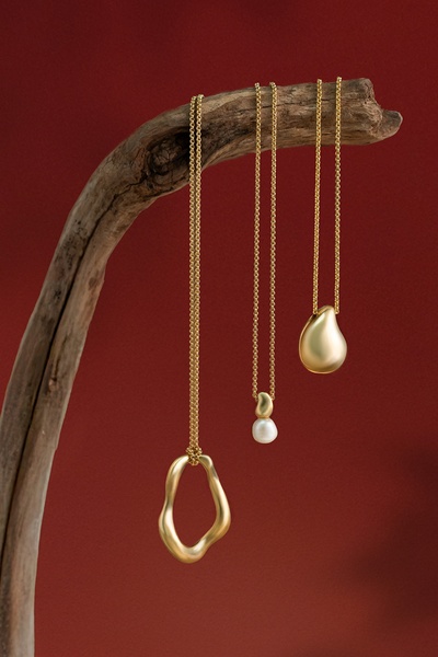 A high-end studio shot of three gold necklaces hanging from a textured wooden branch against a deep red backdrop.