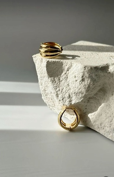 A high-contrast hero shot of gold hoop earrings resting on raw white stone, emphasizing texture and luxury.