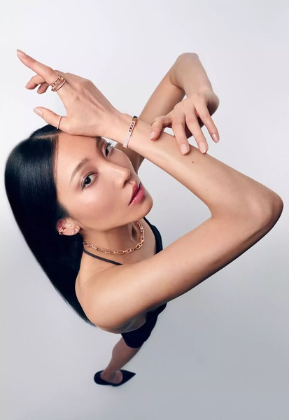 A high-angle, close-up fashion shot featuring a model elegantly posing to showcase layered jewelry pieces on a clean, light-toned background.
